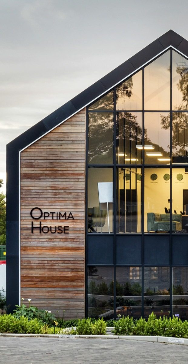 Optima House at dusk, with a timber-clad gable and illuminated double-height glazing